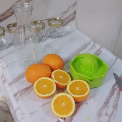 סחטן הדרים ידני ירוק לצד תפוזים חצויים וכוסות זכוכית שקופות עם עיטור זהב על משטח שיש